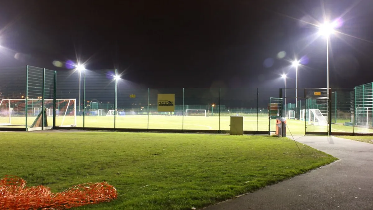 An all-weather pitch at night: the grassroots end of the same fixture list.